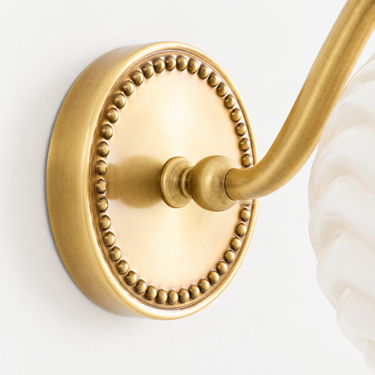 Beaded antique-brass wall plate and curved arm beside the cream shade